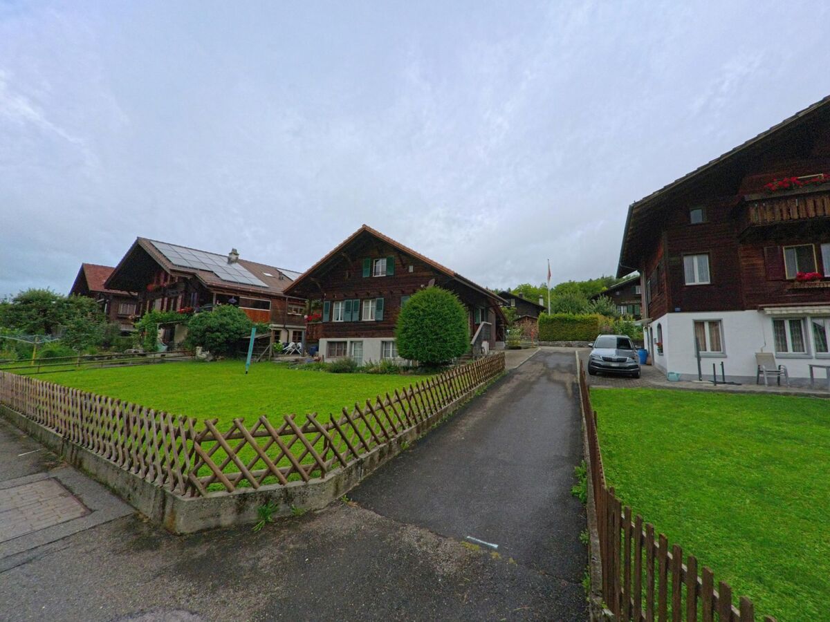 In Hofstetten bei Brienz (3858, Kanton Bern) stehen mehrere traditionelle Holzhäuser mit gepflegten Gärten entlang eines schmalen Zugangswegs zwischen niedrigen Holzzäunen.