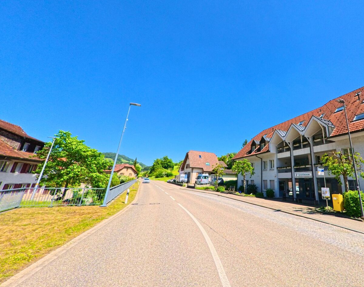 In Holderbank (PLZ 4718, Kanton Solothurn) steht ein laengliches Wohn- und Geschaeftshaus mit charakteristischer Dachform direkt an einer leicht ansteigenden Strasse.