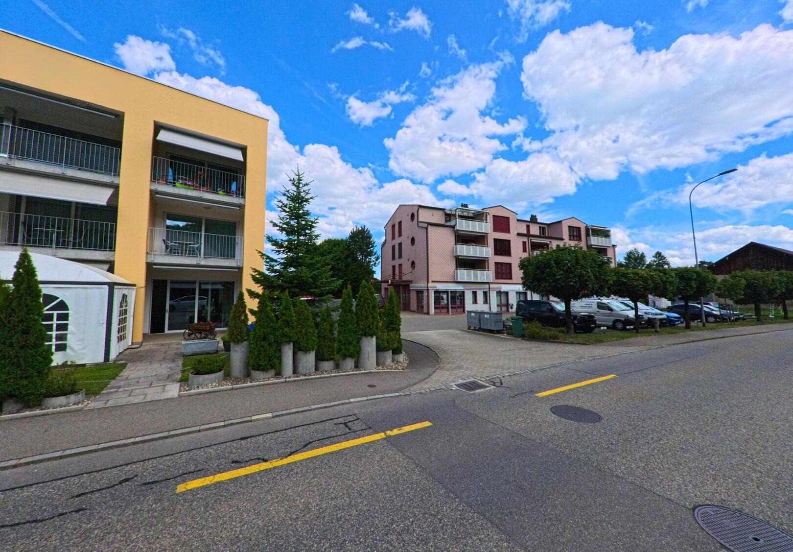 In Holziken (5043, Kanton Aargau) stehen moderne Mehrfamilienhaeuser entlang einer gepflegten Strasse mit Parkplaetzen und Baeumen.
