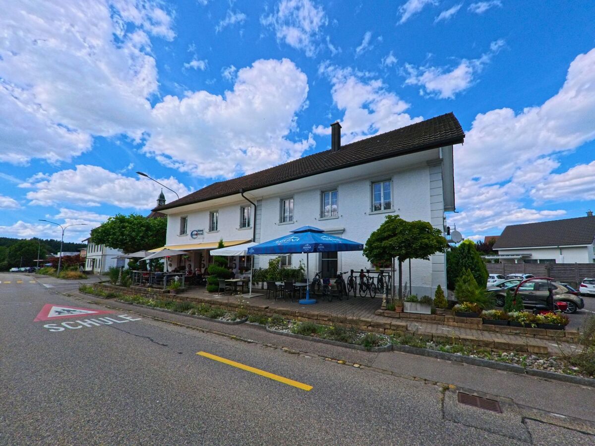 In Holziken (5043, Kanton Aargau) liegt ein Restaurant mit Aussenterrasse und Sonnenschirmen direkt an einer Strasse mit Schulhinweis.