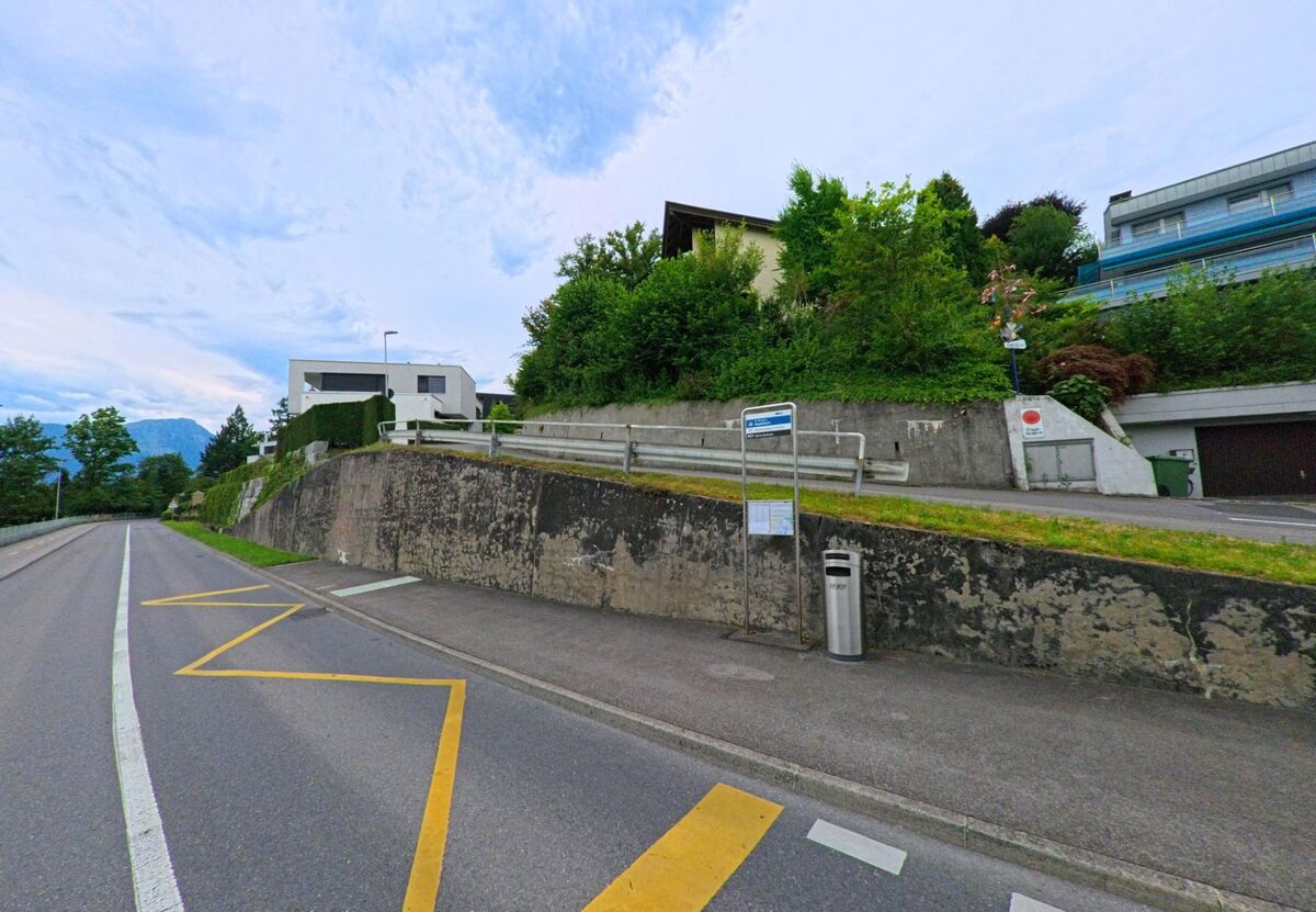In Horw (6047, Kanton Luzern) liegt eine Bushaltestelle an einer leicht ansteigenden Strasse unterhalb mehrerer Wohnhaeuser, die auf einer gestuften Hanglage erbaut sind.
