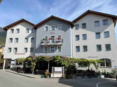 Das Hotel Arkanum in Salgesch (3970, Kanton Wallis) ist ein helles mehrstöckiges Gebäude mit Balkonblumen und einer Terrasse, die von Reben überrankt wird.