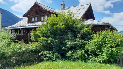 Hinter dichtem Gruen erhebt sich das traditionelle Holzgebaeude des Hotel Hospezi in Trun (7166, Kanton Graubuenden) mit markantem Dach und Balkonen.