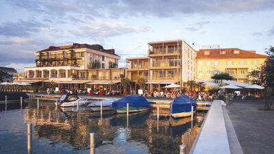 In Lachen (8853, Kanton Schwyz) liegt das Hotel Marina direkt am Hafenbecken, mit moderner Fassade, Sonnenterrassen und Booten im Vordergrund.