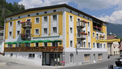 In Müstair (7537, Kanton Graubuenden) steht das traditionsreiche Hotel Muensterhof mit seiner gelben Fassade, verzierten Balkonen und Blumenschmuck.