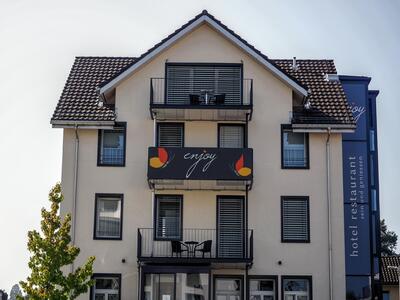 Das Hotel Restaurant Enjoy in Goldach (9403, Kanton St. Gallen) ist ein modernes Gebäude mit Balkonen und einer klaren Fassade, auf der das Logo „enjoy“ prangt.