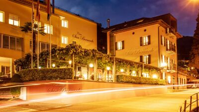 Das Hotel San Bernardo in Contra (6646, Kanton Tessin) leuchtet abends warm im Licht, mit bepflanzter Terrasse und einladender Atmosphäre an einer ruhigen Strasse.