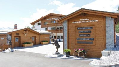 Das Hotel Sarain in Lantsch/Lenz (7083, Kanton Graubuenden) zeigt eine einladende Anlage mit Holzfassaden, Balkonen und einer dekorativen Steinbockskulptur.