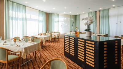 Im Hotel Unione in Bellinzona (6500, Kanton Tessin) praesentiere sich ein helles Restaurant mit gedeckten Tischen, gruenen Stuehlen und grossen Fenstern mit mintfarbenen Vorhaengen.