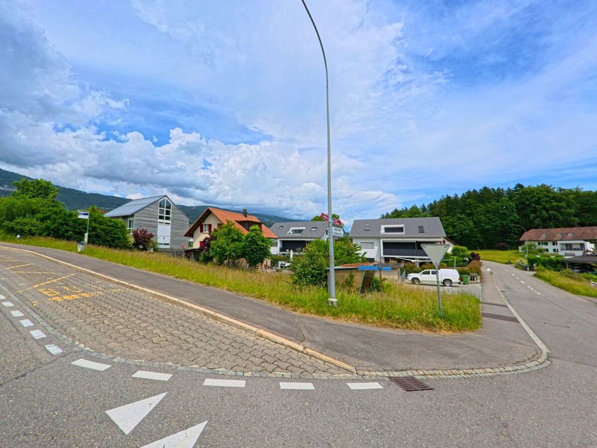 Eine Strassenkreuzung in Hubersdorf (4535, Kanton Solothurn) fuehrt an modernen Wohnhaeusern und einer Bushaltestelle vorbei.