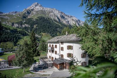 In Spluegen (7435, Kanton Graubuenden) liegt die Hueschera Lodge inmitten einer alpinen Landschaft mit Blick auf bewaldete Haenge und steile Berggipfel.