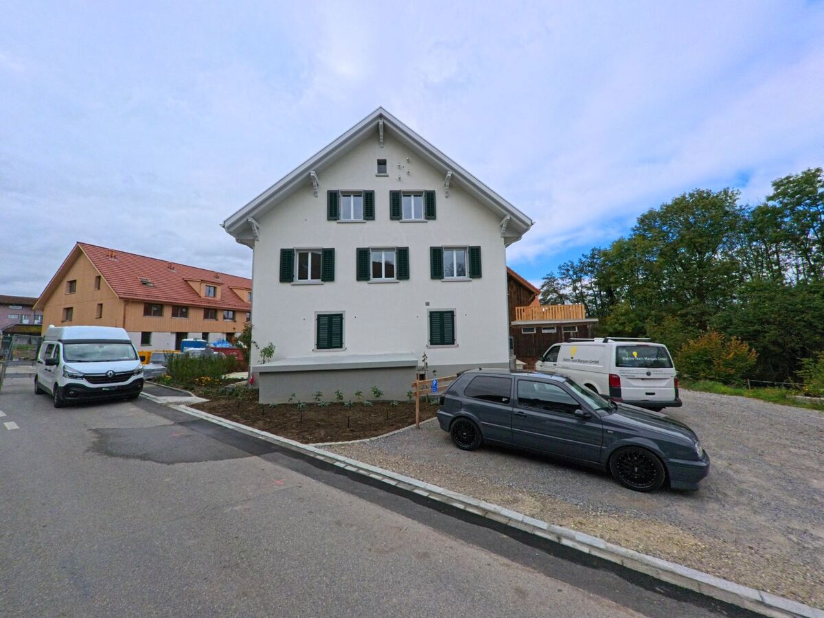 Vor einem hellen Wohnhaus in Hüttwilen (8537, Kanton Thurgau) stehen mehrere Fahrzeuge auf einem neu angelegten Vorplatz neben einer Baustelle.