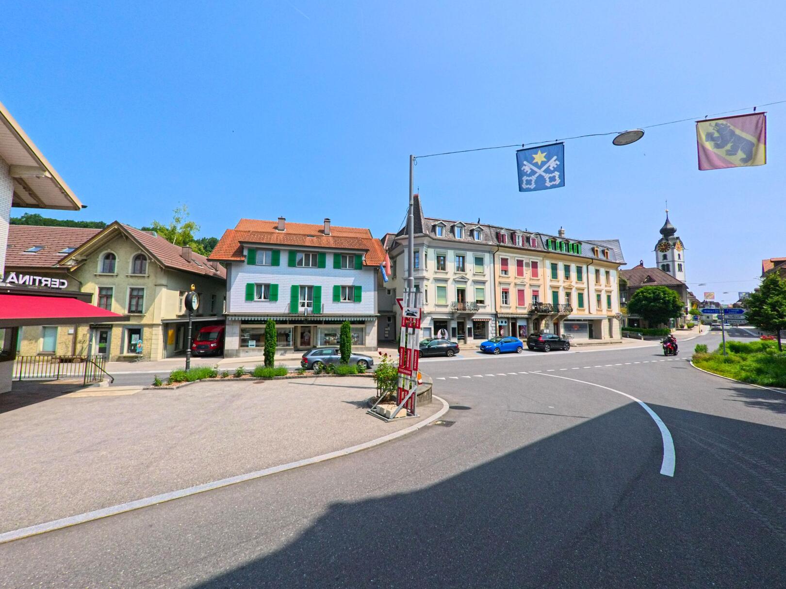 In Huttwil (4950, Kanton Bern) verläuft eine breite Strasse an historischen Gebäuden entlang, mit dem Kirchturm im Hintergrund und festlich geschmückten Strassen.