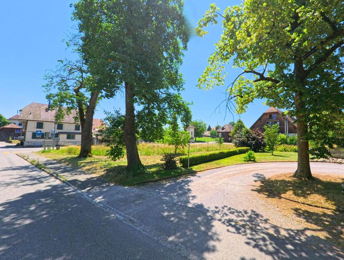 Eine ruhige Ecke in Iffwil (3305, Kanton Bern), gesäumt von Bäumen, mit einem großen Rasenstück und modernen Gebäuden im Hintergrund.