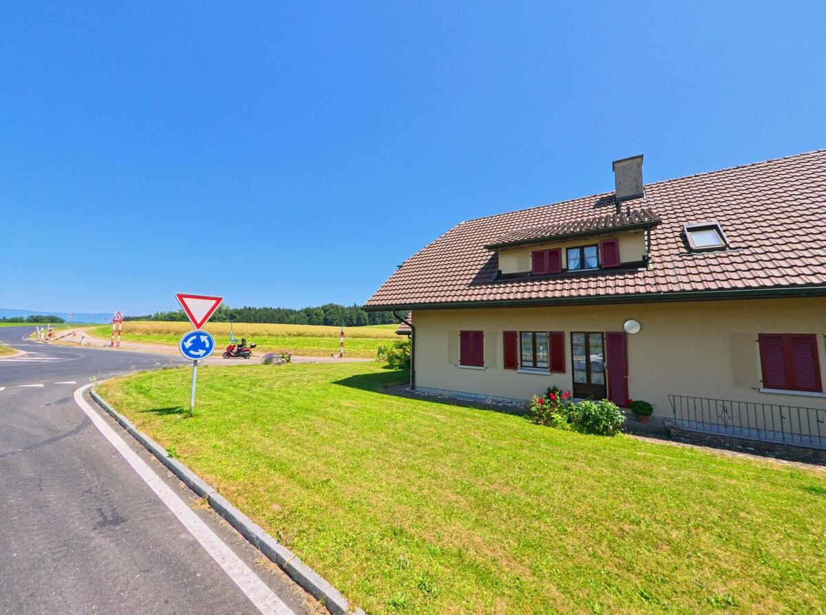 Ein Haus in Iffwil (3305, Kanton Bern) steht an einer Straßenkreuzung, neben einem Kreisverkehr und weiten Feldern.