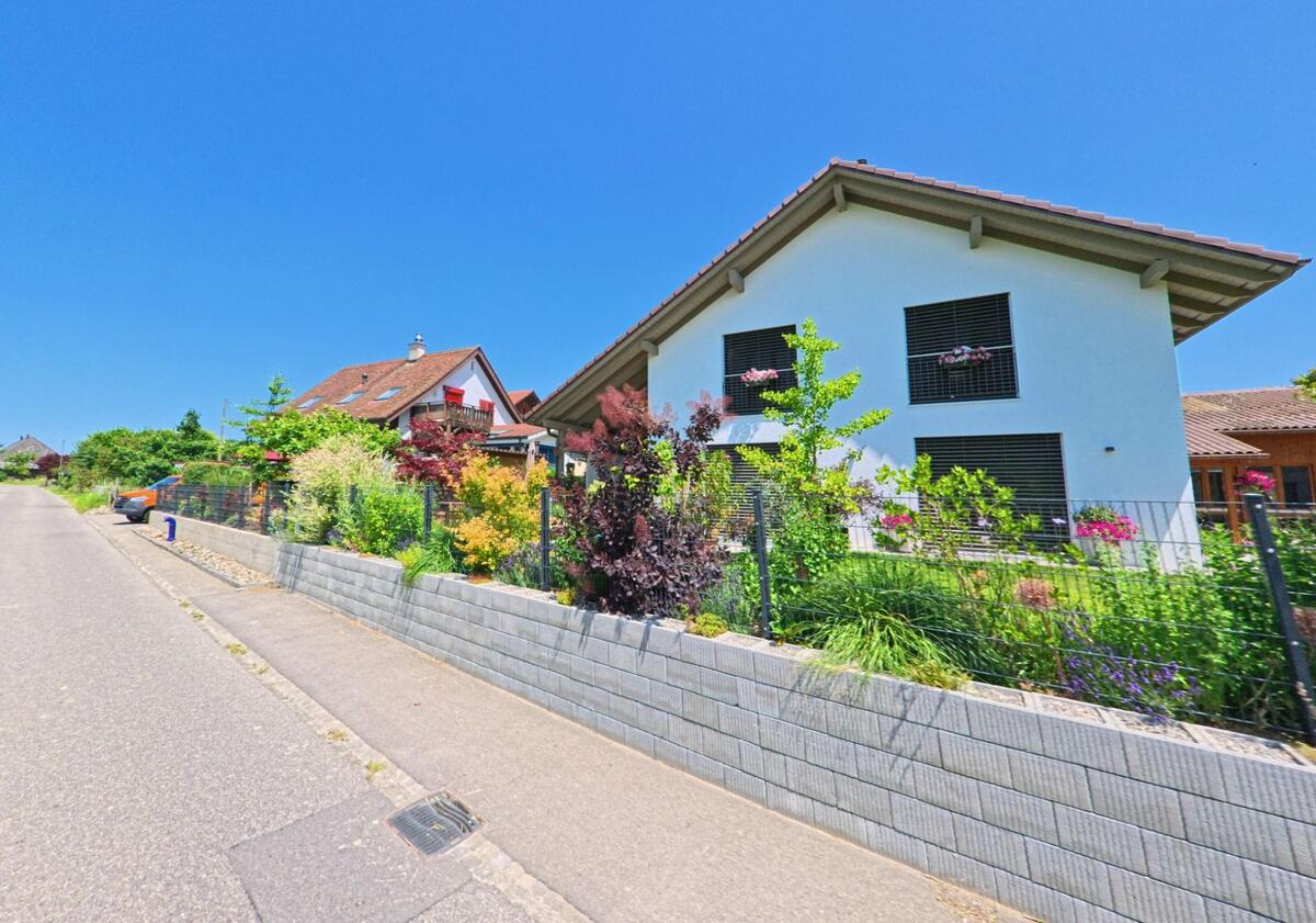Ein modernes Haus in Iffwil (3305, Kanton Bern), umgeben von einem schönen Garten mit bunten Blumen und grünen Pflanzen.