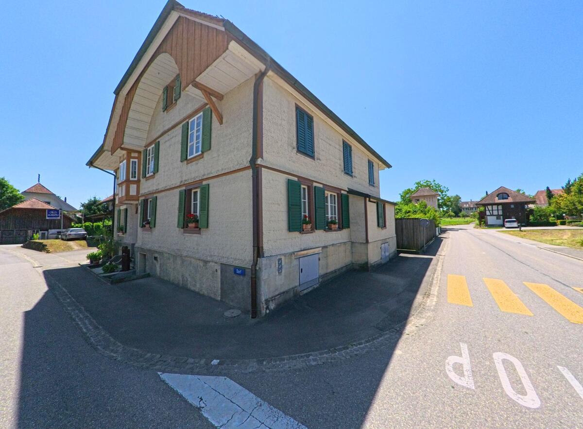 Ein traditionelles Gebäude in Iffwil (3305, Kanton Bern) steht an einer Straßenecke, mit schönen Fenstern und einem gepflegten Garten.