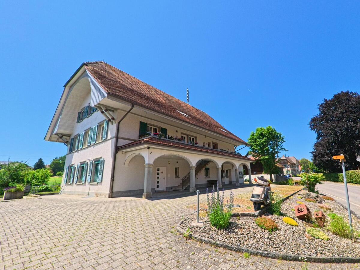 Ein traditionelles Gebäude in Iffwil (3305, Kanton Bern) mit einem großen Vorplatz, gepflegtem Garten und einem Auto vor der Einfahrt.