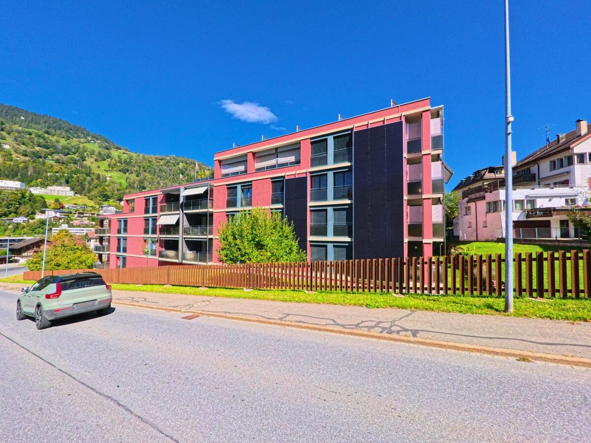 Ein modernes Wohngebäude mit grossen Fenstern und Solarpanels steht in Ilanz (7130, Kanton Graubünden) am Hang unterhalb grüner Wälder.