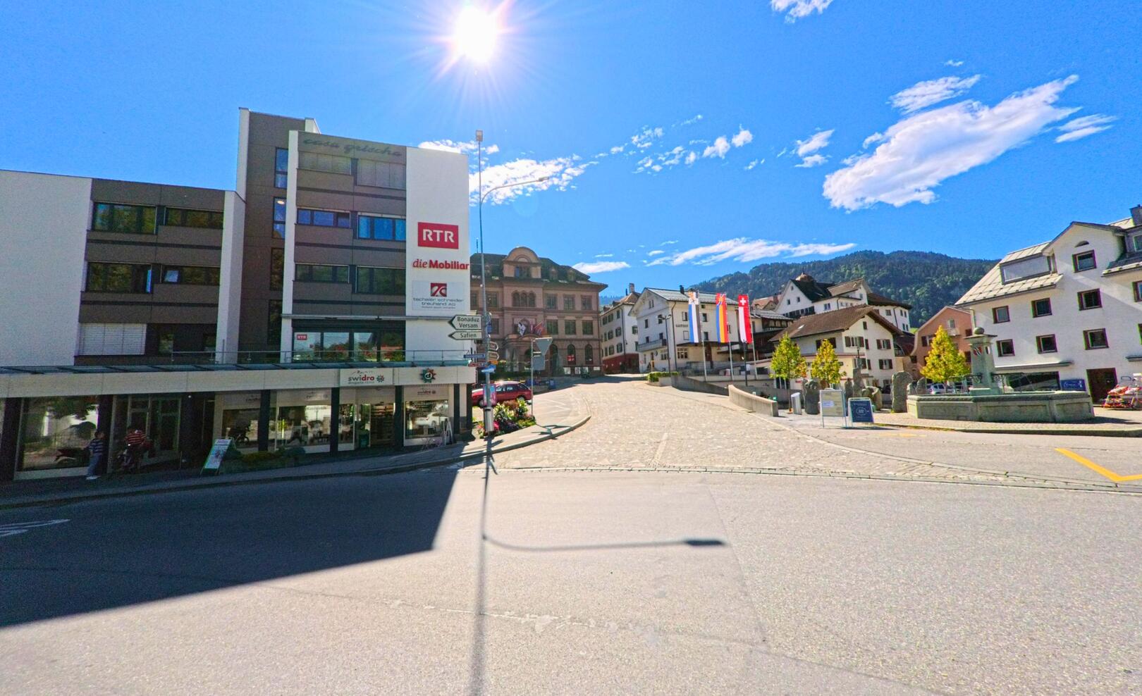 Unter strahlend blauem Himmel zeigt sich das Zentrum von Ilanz (7130, Kanton Graubünden) mit modernen und historischen Gebäuden rund um den sonnigen Platz.