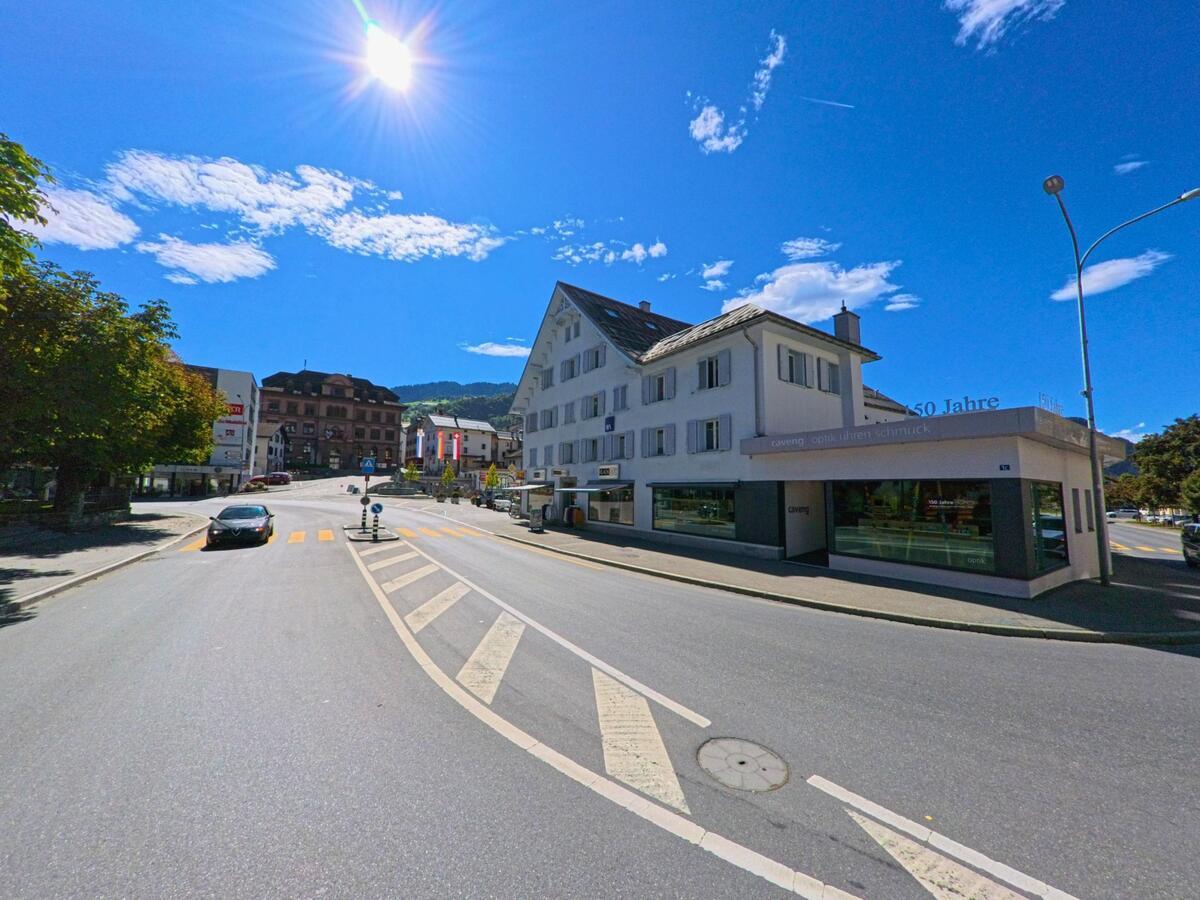 Bei strahlendem Sonnenschein zeigt sich das Zentrum von Ilanz (7130, Kanton Graubünden) mit Geschäften, historischen Gebäuden und einer breiten Strassenkreuzung.