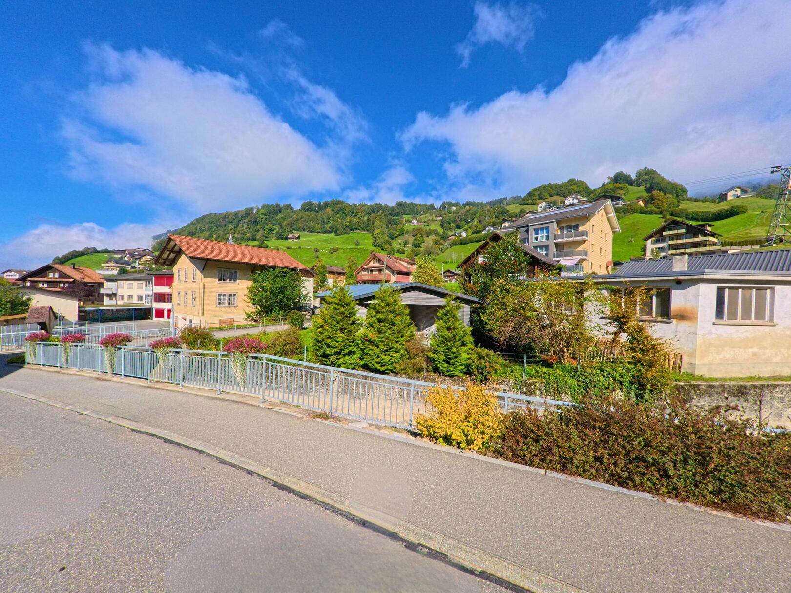 In Illgau (6434, Kanton Schwyz) erstreckt sich ein malerisches Dorfpanorama mit gut erhaltenen Häusern und einer grünen Hügelkulisse im Hintergrund.