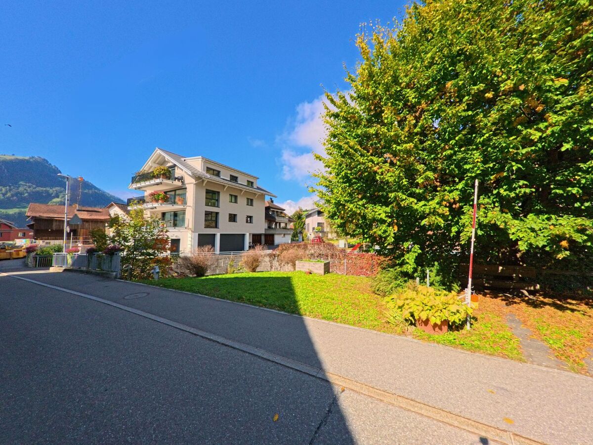 Entlang einer ruhigen Strasse stehen Wohngebäude vor alpiner Kulisse in Illgau (6434, Kanton Schwyz).