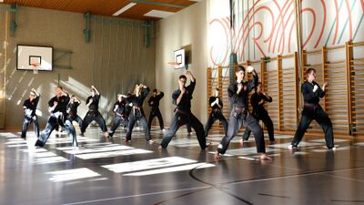 In Uster (8610, Kanton Zuerich) trainiert eine Gruppe des Indonesian Karate Uster in einer hellen Sporthalle synchron verschiedene Techniken in stabilen Standpositionen.