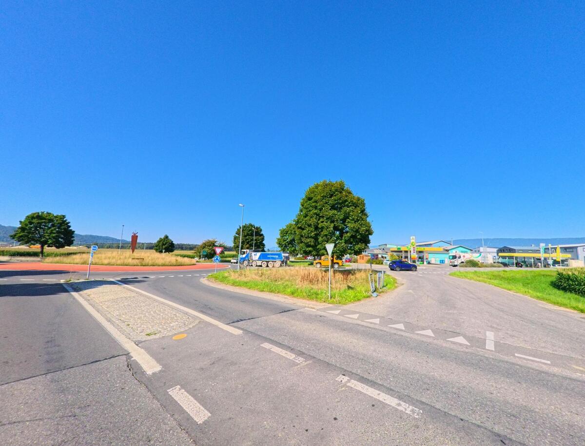 Am Ortseingang von Ins (3232, Kanton Bern) liegt ein Kreisverkehr mit Bäumen und Blick auf eine Tankstelle und Gewerbebauten.