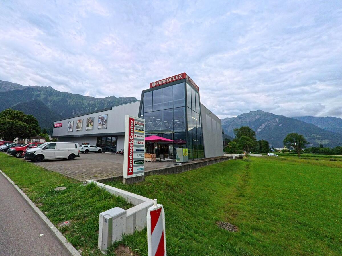 Vor der Kulisse der Berner Alpen steht am Ortsrand von Interlaken (3800, Kanton Bern) ein modernes Gewerbegebäude mit der Aufschrift „Ferroflex“ und angrenzendem Parkplatz.