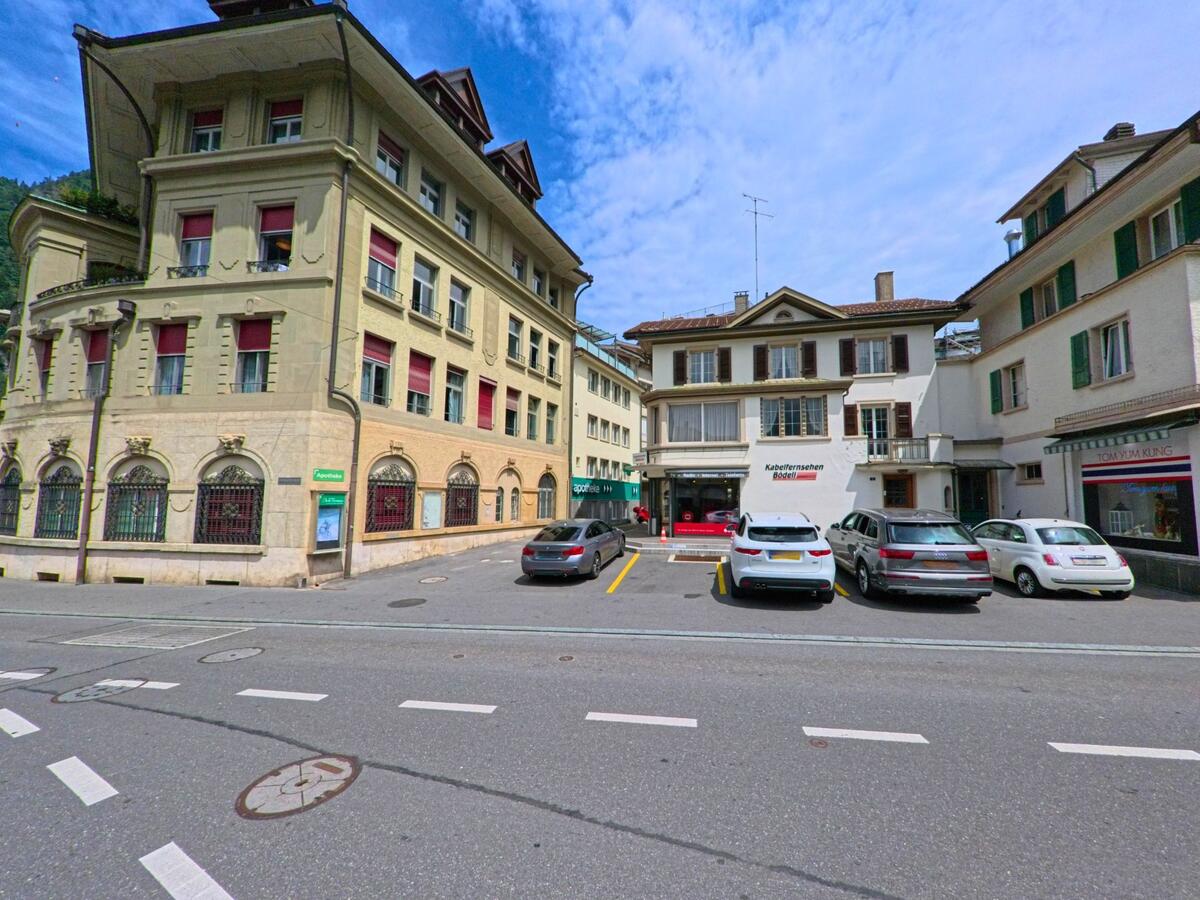 In Interlaken (3800, Kanton Bern) umgeben mehrere Stadthaeuser mit Geschaeften und Parkplaetzen einen kleinen Hof an einer innerstaedtischen Kreuzung.