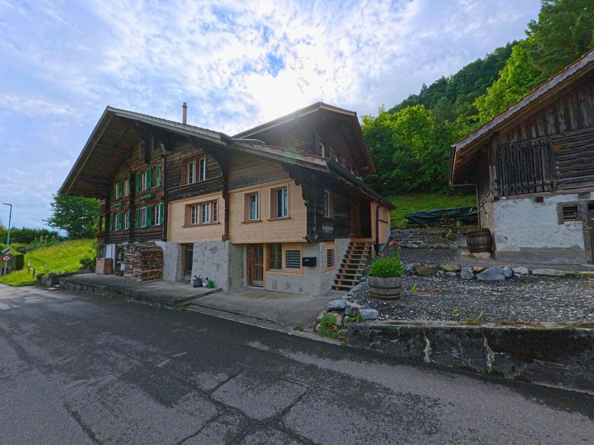 In Iseltwald (3807, Kanton Bern) stehen mehrere historische Holzhäuser mit Schindelfassaden und grünen Fensterläden am Rande eines bewaldeten Hangs.