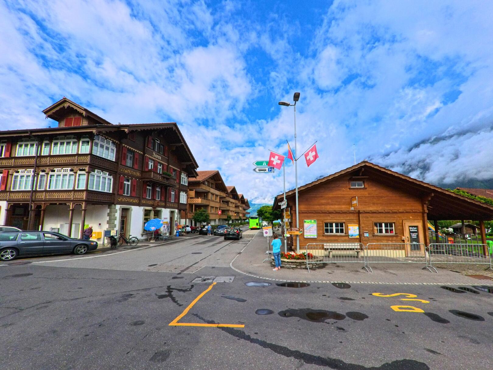 Im Zentrum von Iseltwald (3807, Kanton Bern) treffen traditionelle Holzbauten und ein modernes Tourismusbüro mit Schweizer Fahnen aufeinander.
