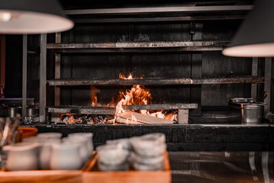 In Feusisberg (8835, Kanton Schwyz) lodert ein offenes Feuer in einer Kuche mit Grillrosten und Metalltoepfen.