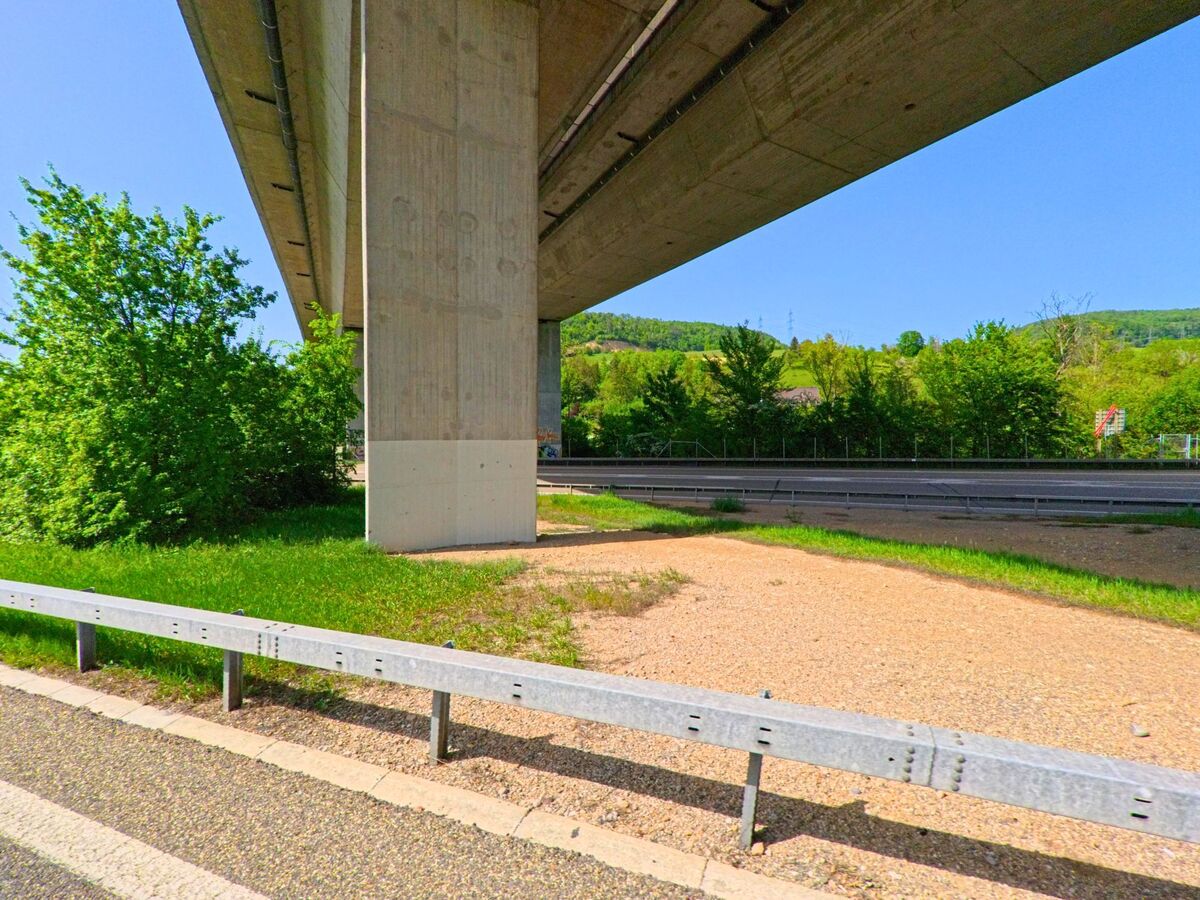 In Itingen (4452, Kanton Baselland) verläuft eine Straße unter einer Brücke hindurch. Der Bereich um die Brücke ist von grünen Büschen und Wiesen umgeben.