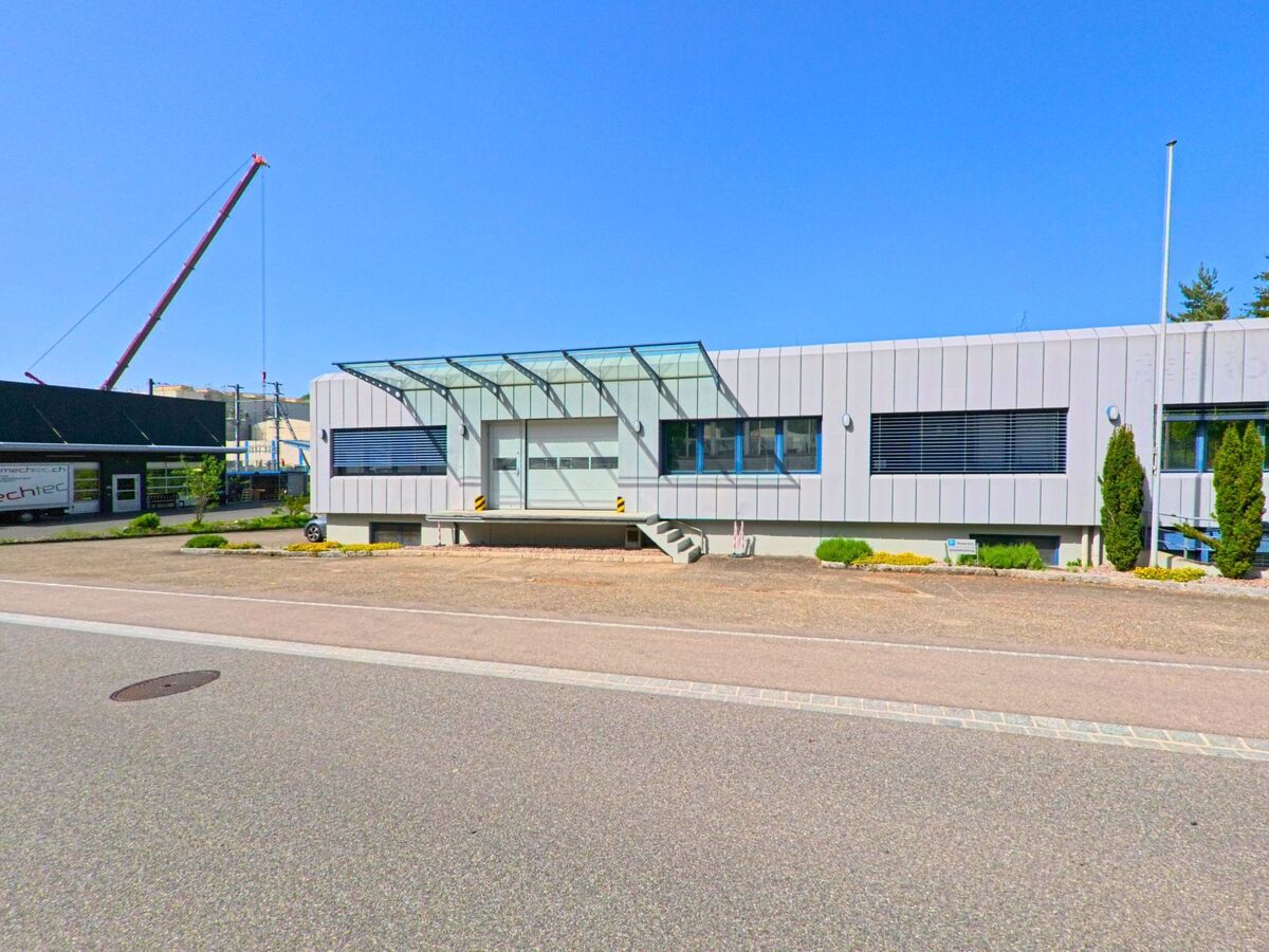 In Itingen (4452, Kanton Baselland) ist ein modernes Gebäude mit Glasdach und einem Kran im Hintergrund zu sehen. Die Straße verläuft am Gebäude entlang.