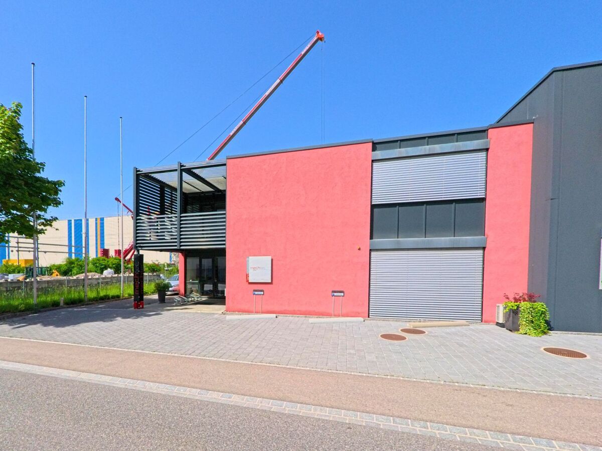 In Itingen (4452, Kanton Baselland) ist ein modernes Gebäude in roter Farbe zu sehen, mit einem Kran im Hintergrund. Die Straße verläuft entlang des Gebäudes.