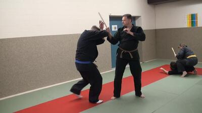 In Liestal (4410, Kanton Baselland) trainieren zwei Teilnehmende von Jiu Jitsu Samurai Liestal realistische Abwehrtechniken mit Stock, waehrend im Hintergrund weitere Uebungen stattfinden.