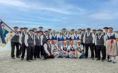Das Jodelchörli am Pfäffikersee posiert in Pfäffikon (8330, Kanton Zürich) in traditioneller Tracht mit Vereinsfahne vor einer offenen Landschaft.