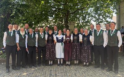 Die Mitglieder des Jodelklubs Gommiswald aus Gommiswald (8737, Kanton St. Gallen) stehen gemeinsam in traditioneller Kleidung unter Bäumen im Freien.