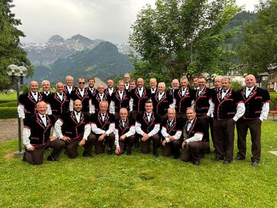 Auf einer Wiese in Oberburg 3414 im Kanton Bern posiert der Jodlerklub in einheitlicher Tracht vor Baeumen und markanter Bergkulisse.