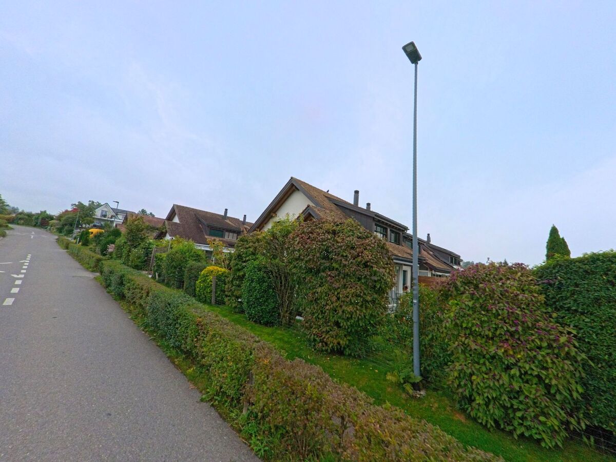 Eine ruhige Quartierstrasse in Jonen (8916, Kanton Aargau) verläuft entlang gepflegter Reihenhäuser mit grünen Hecken und Vorgärten.