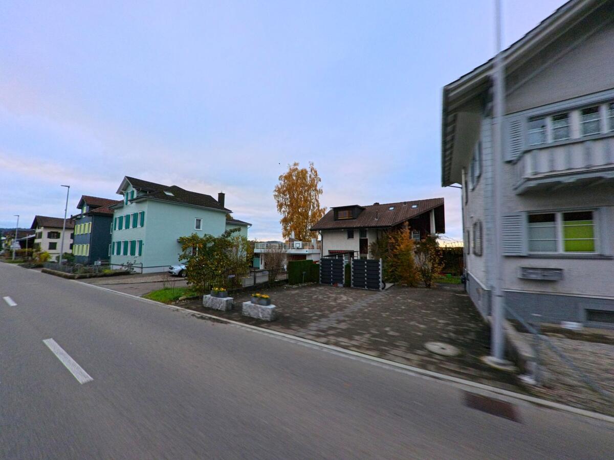 In Jonschwil (9243, Kanton St. Gallen) stehen entlang der Strasse mehrere Wohnhaeuser, darunter ein mintfarbenes Mehrfamilienhaus und ein dunkleres Einfamilienhaus mit Hofzufahrt.