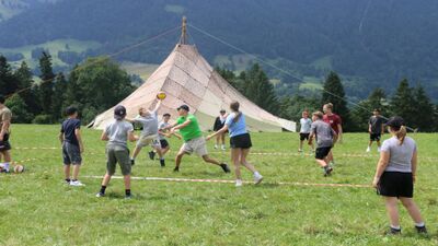 Kinder spielen gemeinsam mit einem Ball auf einer Wiese vor einem grossen Zelt in Triengen (6234, Kanton Luzern) waehrend eines aktiven Lagerspiels im Freien.