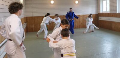 In Dietikon (8953, Kanton Zuerich) ueben Kinder im Dojo des Judo Sportclubs Dietikon verschiedene Wurftechniken, begleitet von einem Trainer im blauen Gi.