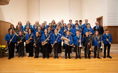 Die Mitglieder der Jugendmusik Konolfingen aus Konolfingen (3510, Kanton Bern) posieren gemeinsam in blauen Uniformen mit verschiedenen Blas- und Schlaginstrumenten für ein Gruppenfoto.
