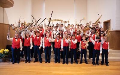 Die Jugendmusik präsentiert sich in Unterseen (3800, Kanton Bern) in Uniform mit zahlreichen Blasinstrumenten für ein gemeinsames Gruppenfoto auf einer Bühne.