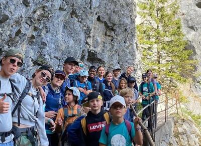 Mitglieder der Jungwacht und Blauring Hinwil unternehmen eine gemeinsame Wanderung entlang eines schmalen Bergwegs in einer Felslandschaft. Kinder, Jugendliche und Leitende posieren auf dem Weg vor steilen Felswänden und tragen Rucksäcke sowie Outdoor-Bekleidung. Die Aufnahme zeigt eine Vereinsaktivität der Jungwacht und Blauring Hinwil in Hinwil (8340, Kanton Zürich).