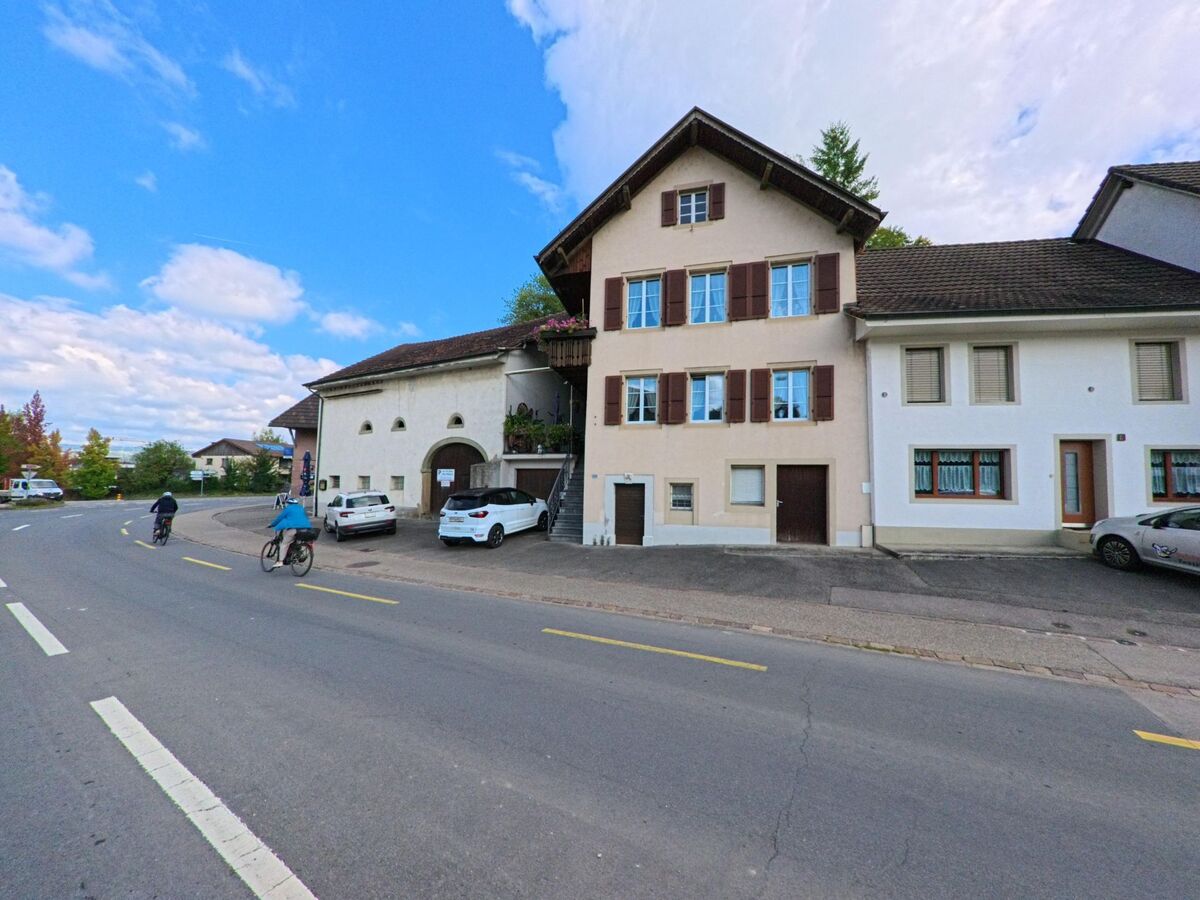 Zwei Radfahrer fahren eine leicht gebogene Strasse entlang, gesäumt von traditionellen Wohnhäusern mit Fensterläden in Kaisten (5082, Kanton Aargau).