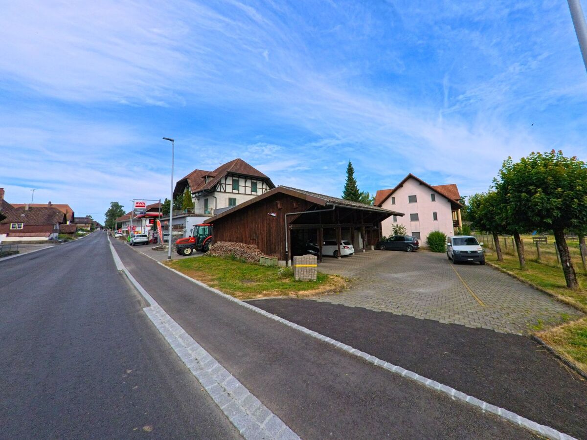 Entlang der Hauptstrasse von Kallnach (3283 im Kanton Bern) liegen eine Tankstelle, Wohnhäuser und ein Carport mit mehreren Fahrzeugen.